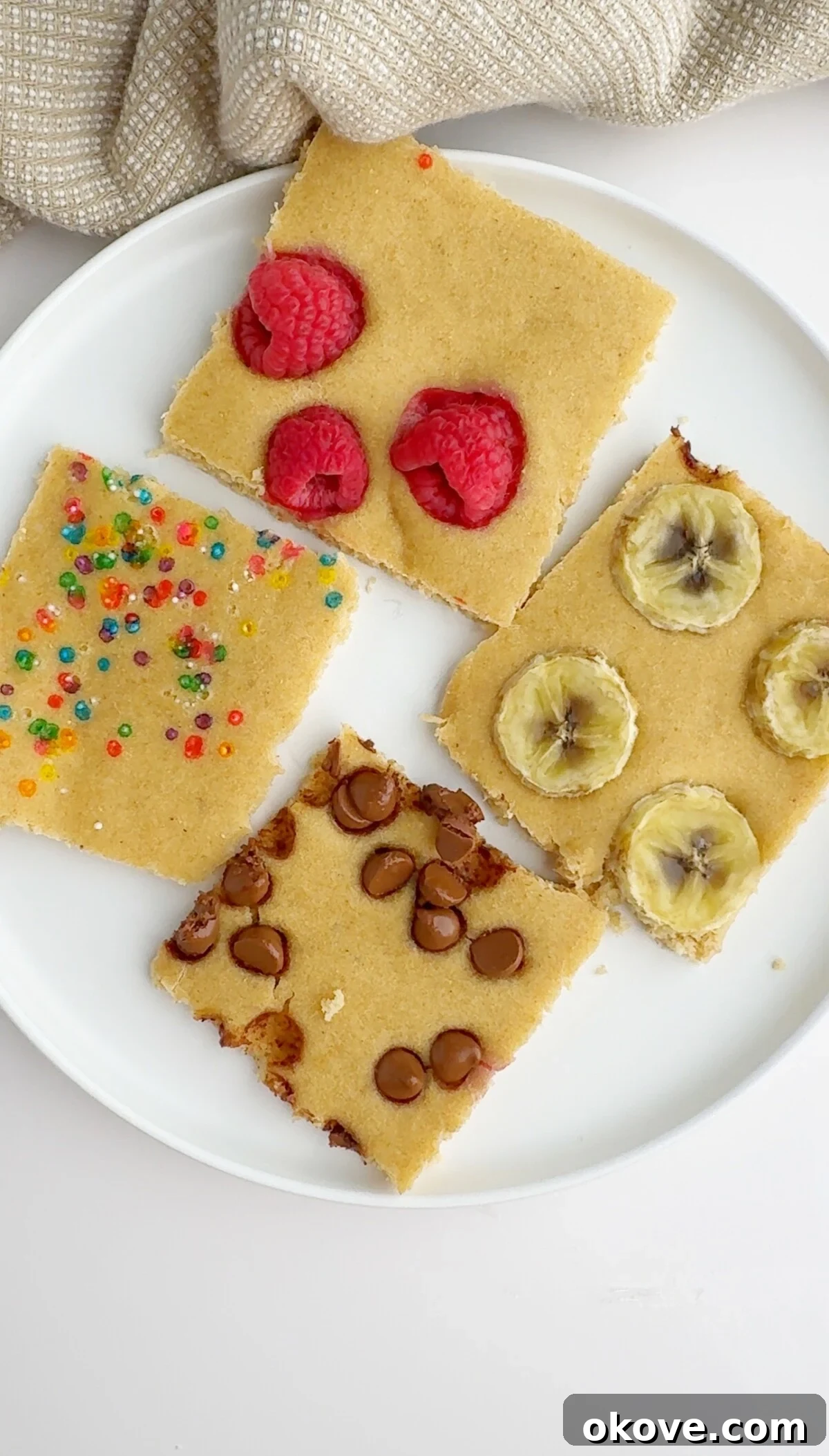 No-Flip Pancakes 2 Sheet pan pancakes on a plate with raspberries, bananas, chocolate chips and sprinkles as toppings