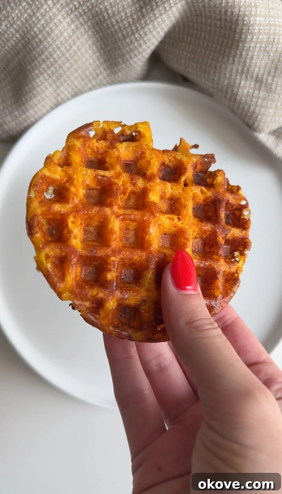 A hand holding a cheesy carrot waffle