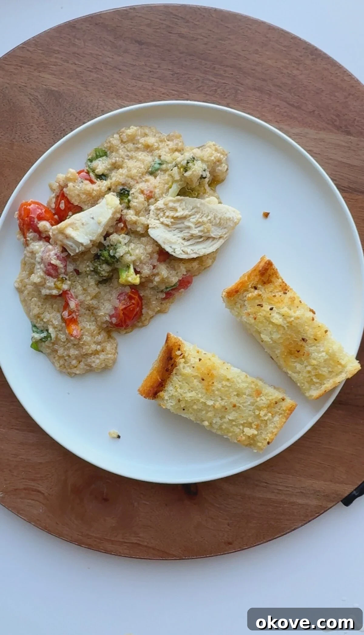 Nourishing Baked Chicken with Quinoa and Vegetables 3 Baked chicken, quinoa, and veggies on a plate with two pieces of garlic bread
