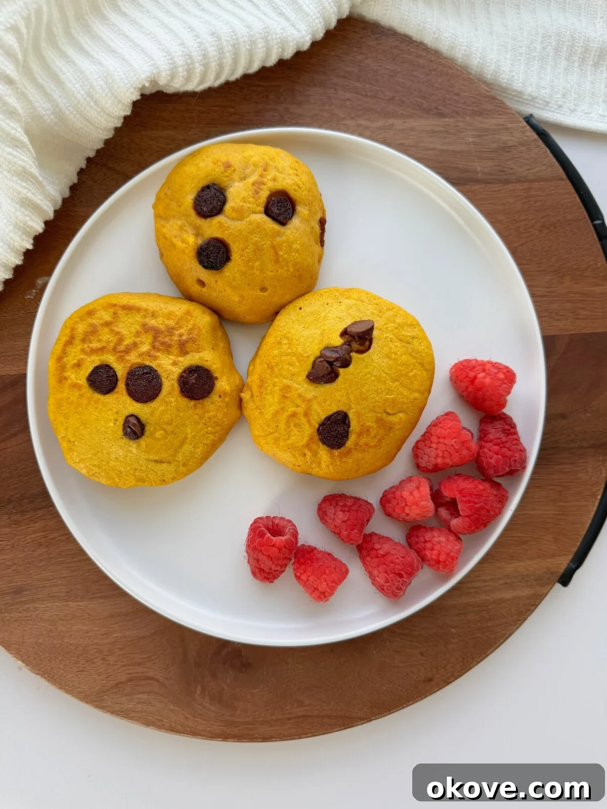 Three pumpkin pancakes on a white plate with some raspberries