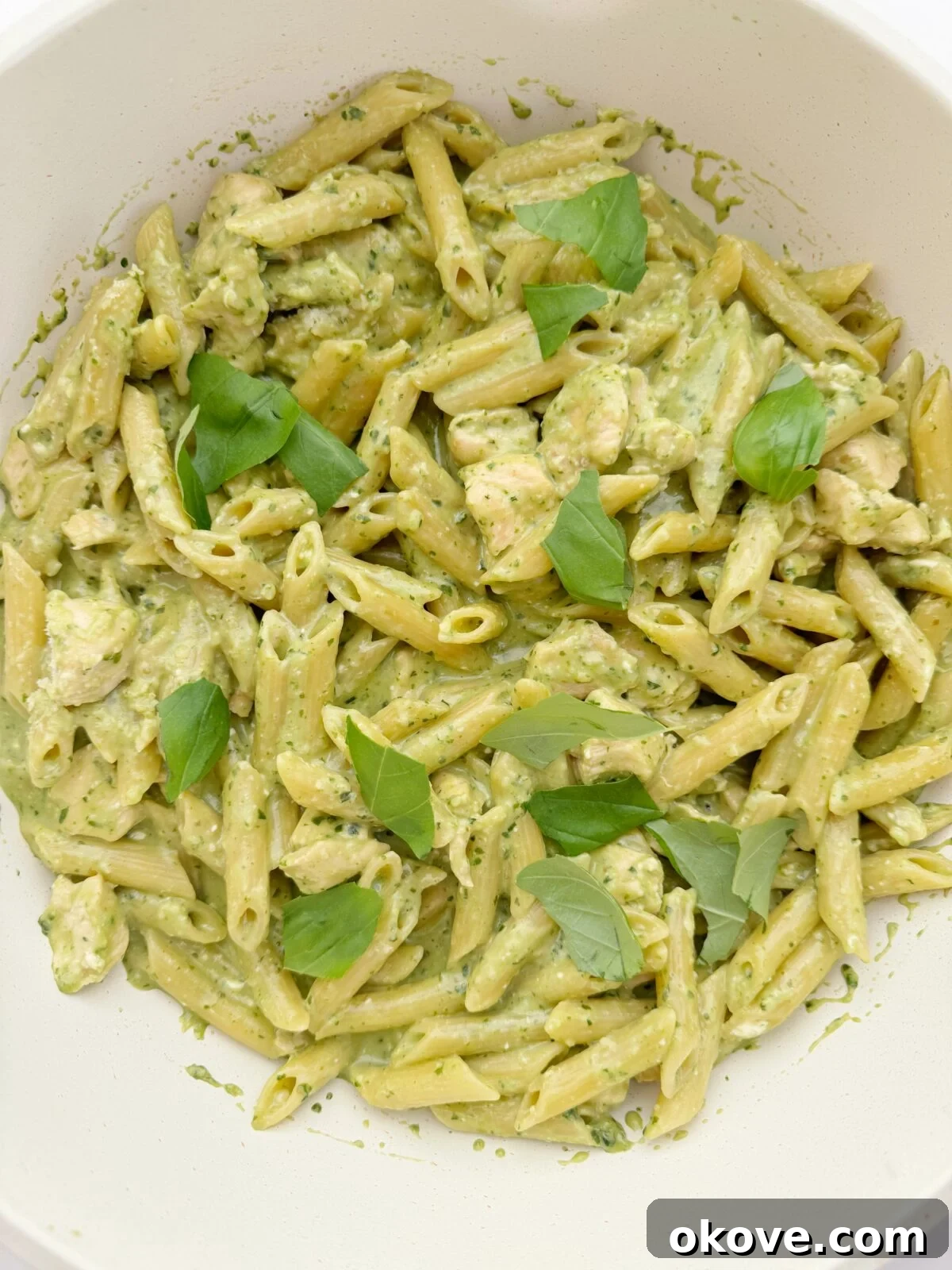 Velvet Pesto Pasta 2 A large white bowl filled with creamy pesto chicken pasta, garnished with fresh basil leaves, ready to be served to a family.