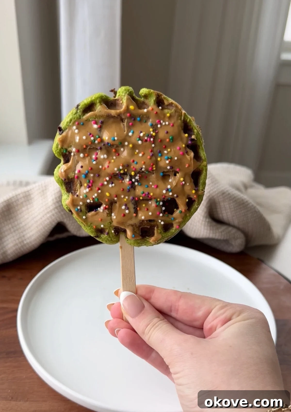 Green Goodness Waffle Pops 2 A spinach waffle pop topped with peanut butter and colorful sprinkles, ready for a toddler to enjoy.