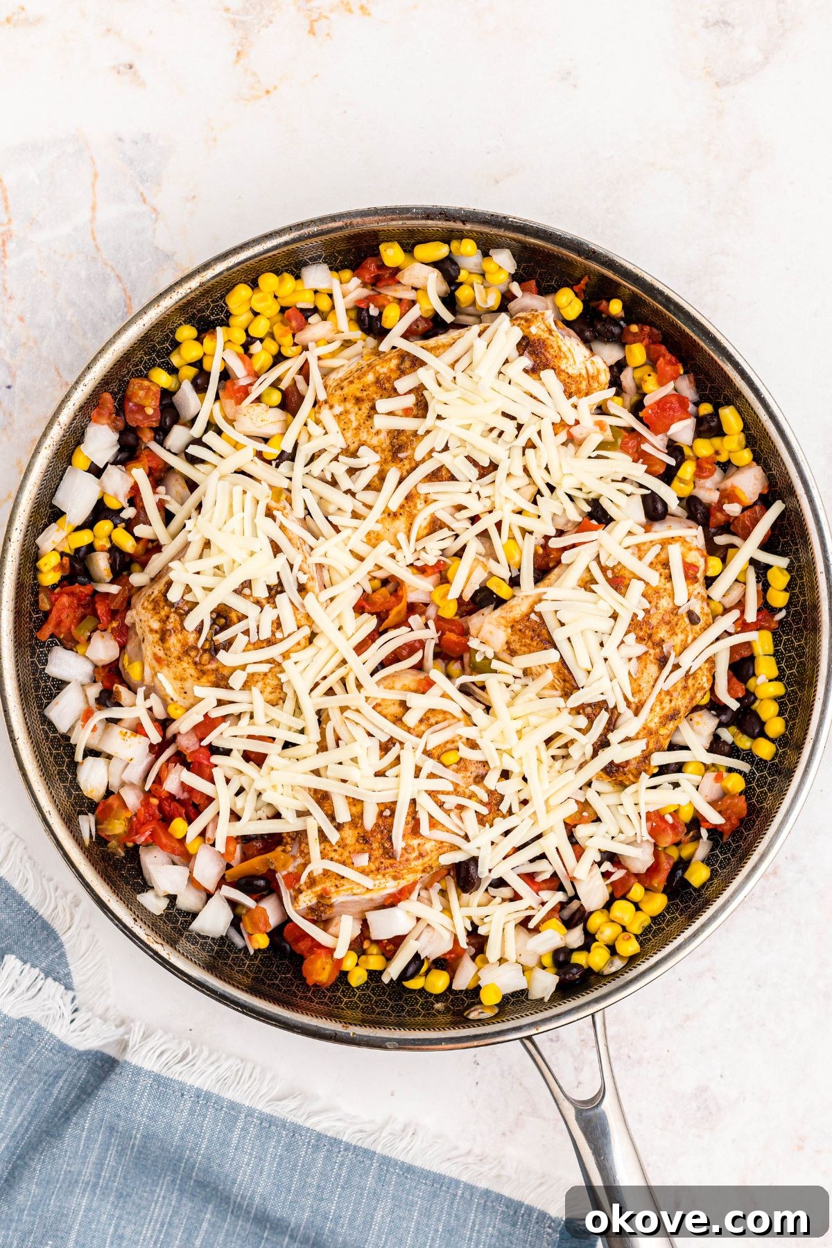 Cheese and chicken mixed with corn and black beans in a large skillet before being cooked.