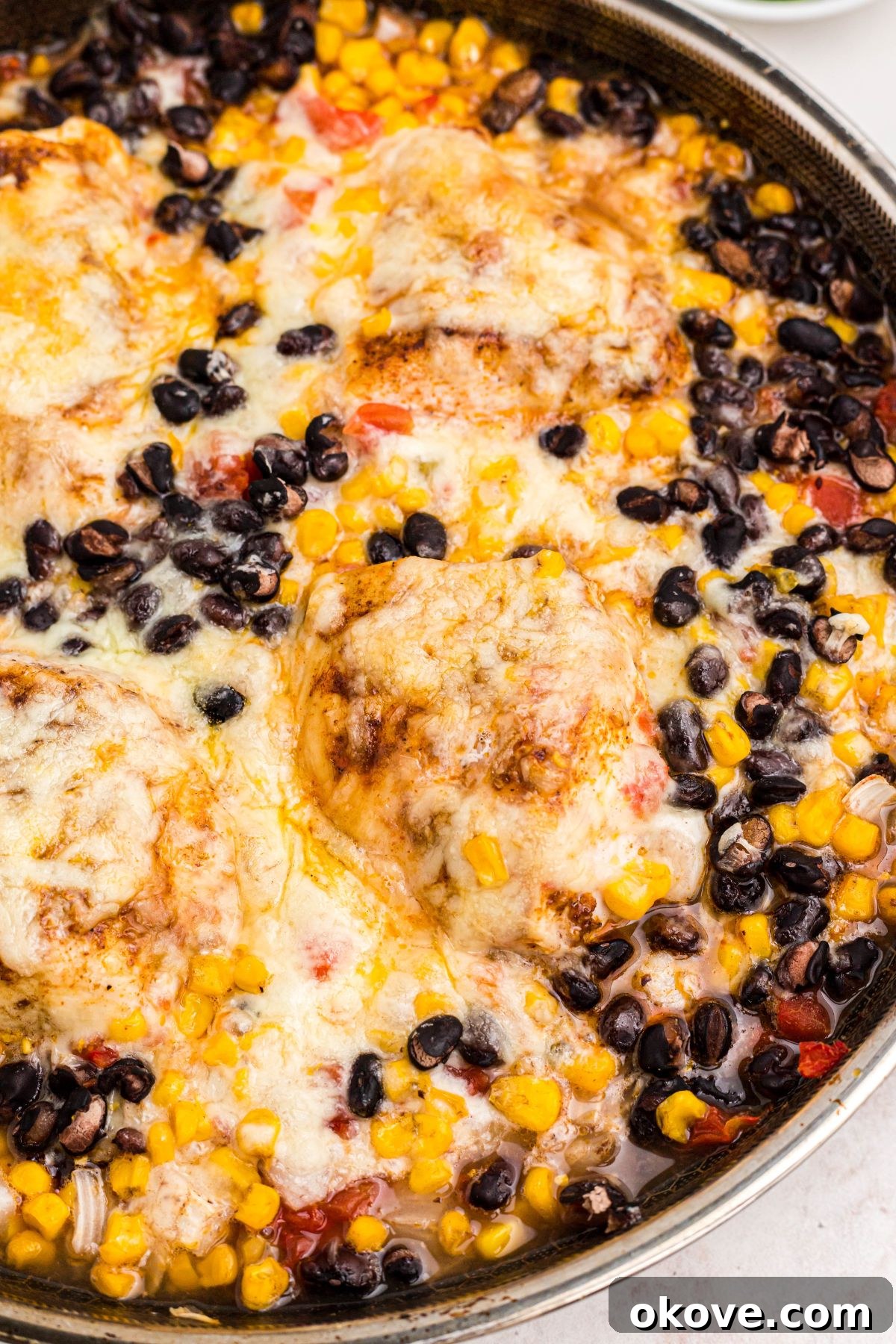 Cheese covered chicken mixed with corn and black beans in a large skillet.