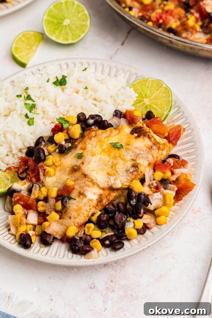 Juicy, cheese chicken surrounded by veggies, and served with rice on a white plate. 