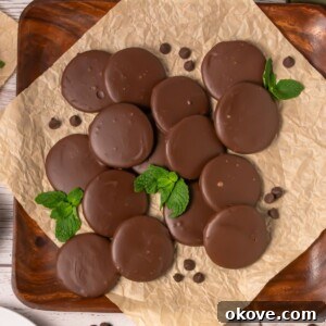 Thin chocolate coated cookies, on brown parchment paper, with a few mint leaves on the paper with the cookies.