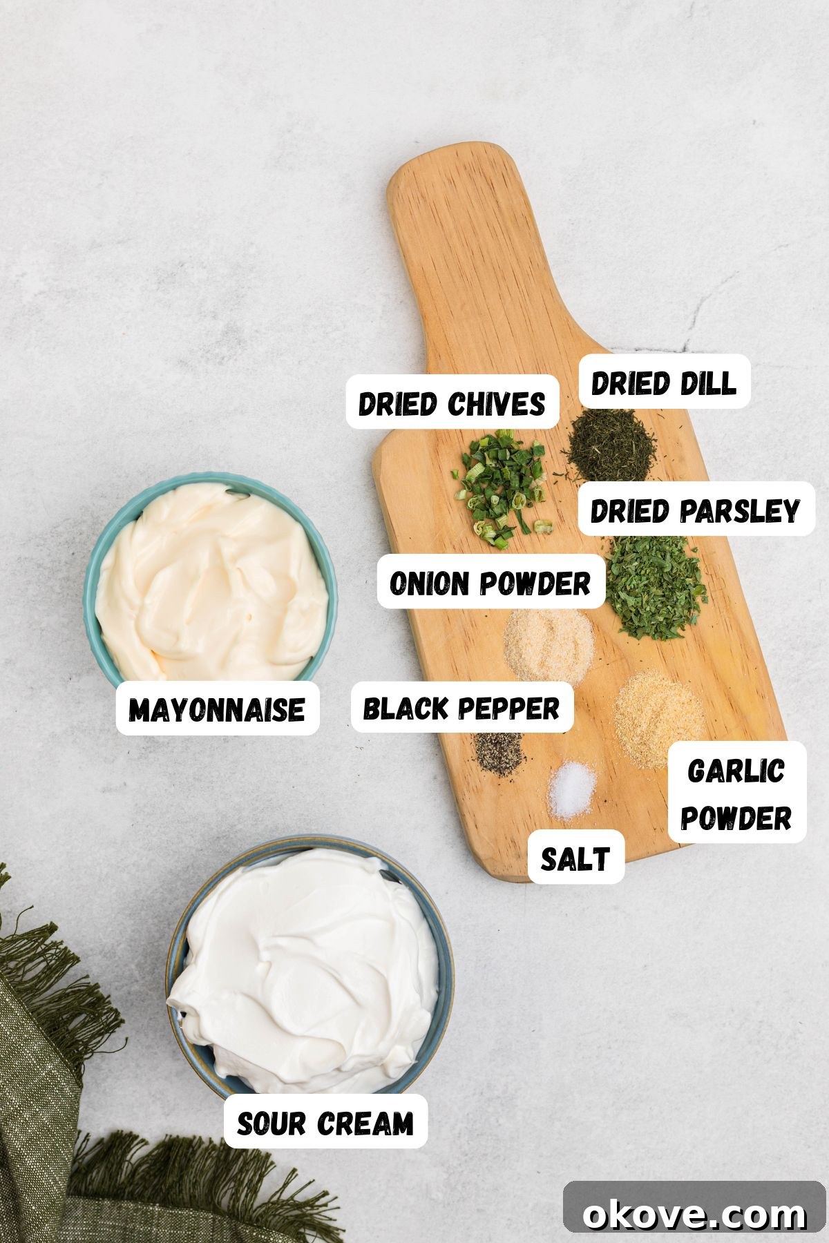 Creamy Ranch Dip 3 Individual ingredients neatly arranged and labeled on a rustic cutting board: a bowl of mayonnaise, a bowl of sour cream, and small piles of dried dill, parsley, garlic powder, onion powder, salt, and black pepper, ready to be combined for the ranch dip.