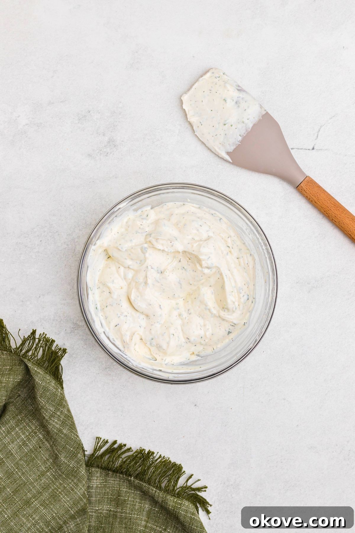 Creamy Ranch Dip 6 The creamy ranch dip is fully mixed in a clear glass bowl, showcasing a smooth, well-combined texture with visible flecks of green herbs, indicating it's ready for chilling.