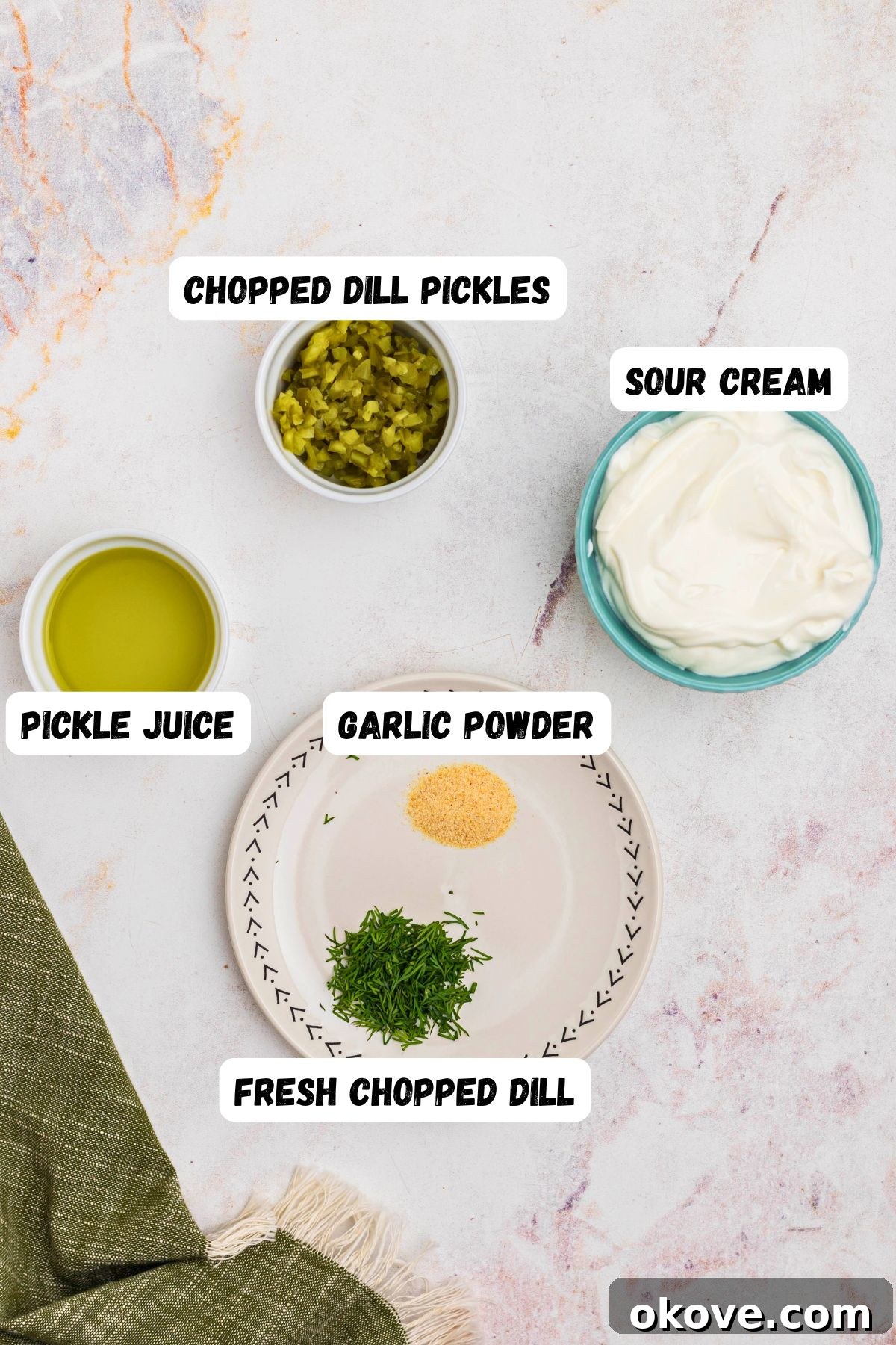 Chopped pickles, sour cream, pickle juice, and seasonings, measured out and labeled, on a marble table. 
