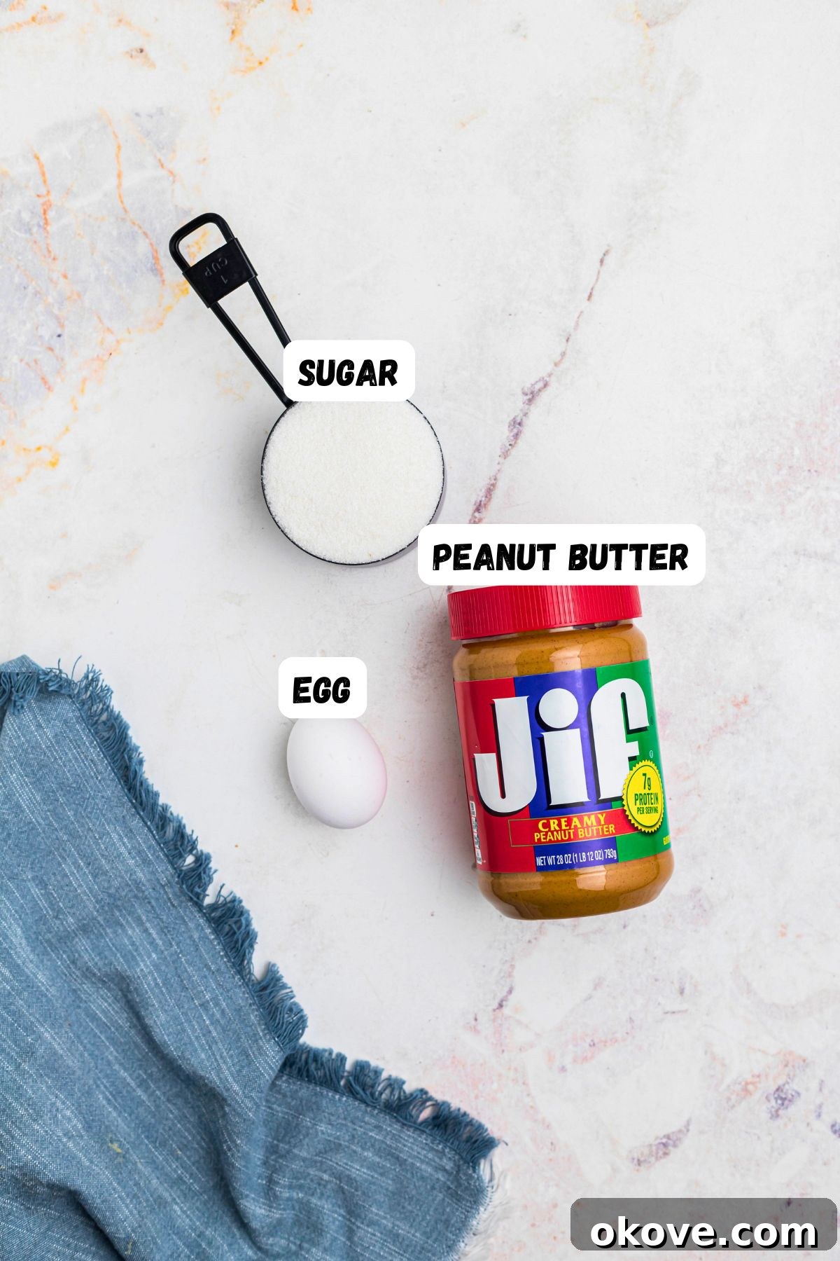 Effortless 3 Ingredient Peanut Butter Bliss 3 Peanut butter, sugar, and an egg, on a marble table, labeled, next to a blue linen.