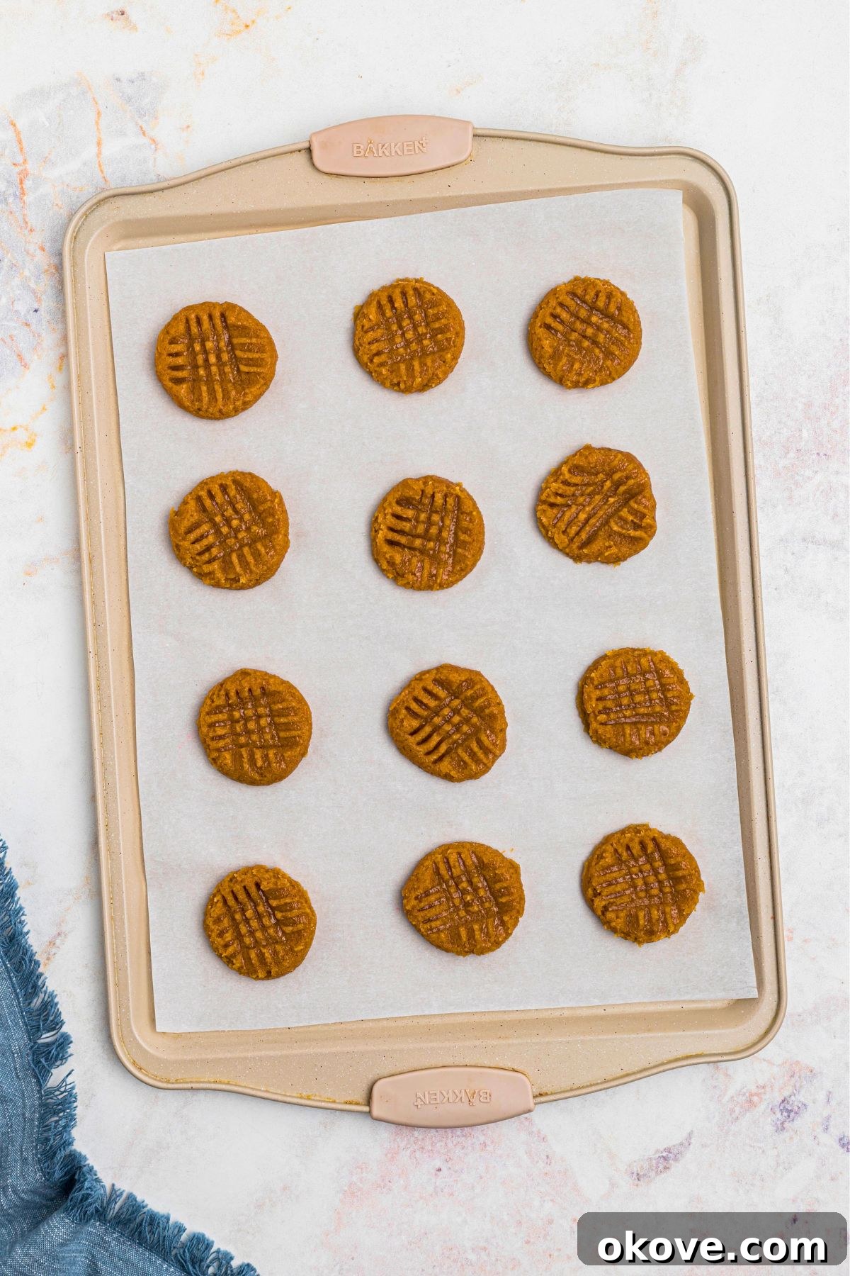 Effortless 3 Ingredient Peanut Butter Bliss 7 Uncooked balls of cookie dough on parchment paper lined baking sheet, pressed down with a fork to make criss cross shape, before baking.