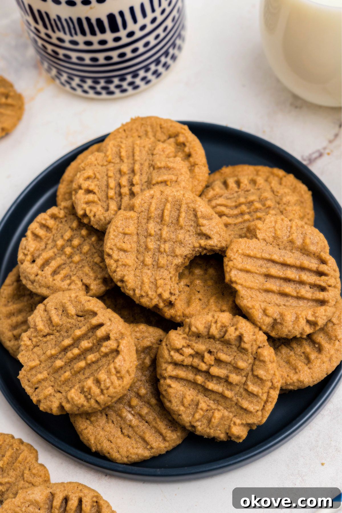 Effortless 3 Ingredient Peanut Butter Bliss 8 Blue round plate filled with a pile of peanut butter cookies with the top cookie missing a bite.