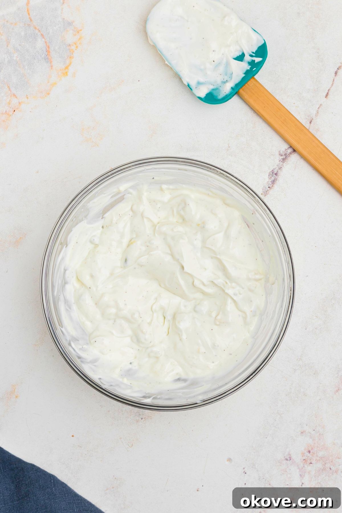 Creamy Blue Cheese Dip 5 A clear glass mixing bowl filled with the newly mixed blue cheese dip, showcasing the even distribution of blue cheese crumbles throughout the creamy base. A rubber spatula rests nearby, ready for serving.