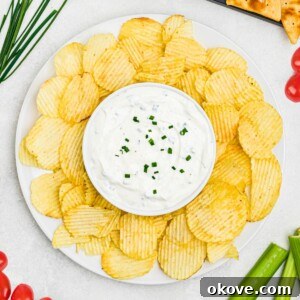 A large plate of crispy potato chips with a small, round bowl of creamy white dip at its center, surrounded by an inviting platter of fresh, colorful vegetables.