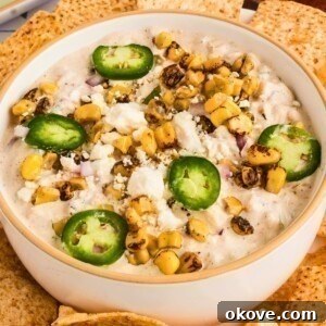 A white bowl showcasing creamy Mexican street corn dip, perfectly garnished and surrounded by an inviting array of tortilla chips, ready for dipping.