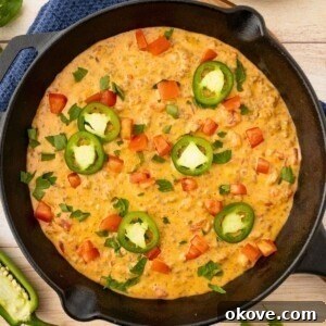 A black skillet filled with bubbly, cheesy dip, artfully garnished with a vibrant topping of chopped tomatoes and finely diced jalapenos for a fresh, spicy kick.