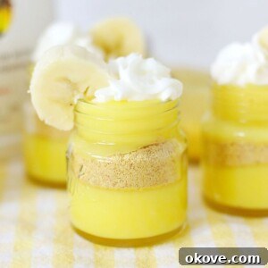 Bright yellow pudding layers in mini jars, topped with whipped cream and garnished with a banana slice.