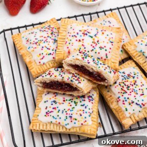 Golden crusted pie crusts, cut into rectangles, filled with strawberry jam, and topped with white icing and sprinkles, on a white rectangle plate.