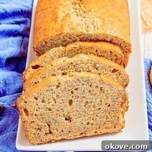 Golden loaf of banana bread on a white rectangle plate, sliced with a banana laying next to the plate.