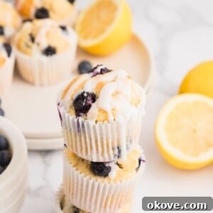 Golden lemon blueberry muffins baked and then stacked on the table with lemons stacked behind the muffins.