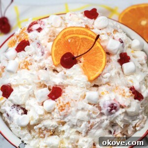 White bowl with fruit salad, topped with cherries and orange slices.