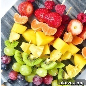 Pieces of fruit skewered in a rainbow color pattern on a small light gray cutting board.