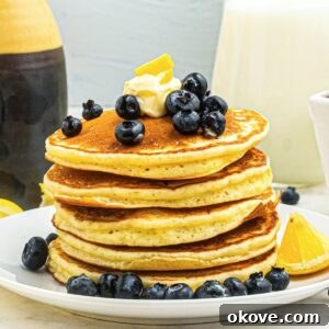 Golden fluffy pancakes stacked on a white plate, topped with blueberries and butter.