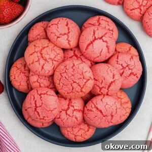 Pink strawberry cake mix cookies stacked on a blue plate in front of bowls of strawberries.