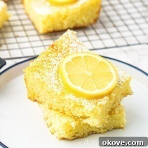 Bright yellow lemon bars stacked on a small white plate with a slice of lemon on top.