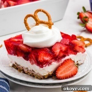 Layers of strawberry jello, pretzel crust and cream cheese filling, on a black plate.