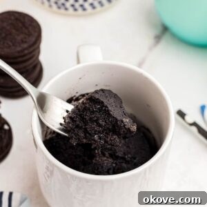 Chocolate mug cake with a bite scooped out on a fork with Oreos and milk on the table.