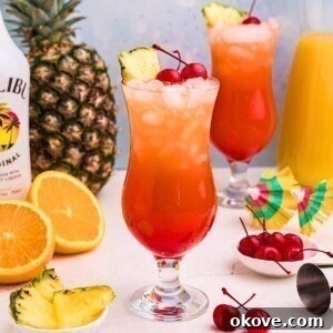 Red and orange drink mixed together in a hurricane glass with orange slices and cherries on the marble table.