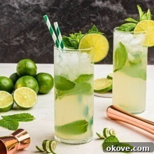 Bright yellow drink in a tall chilled glass, with two green striped straws, with limes and lime curls on the marble table.