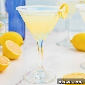 Lemon drop martini in a martini glass on a marble table with lemon slices on the table.