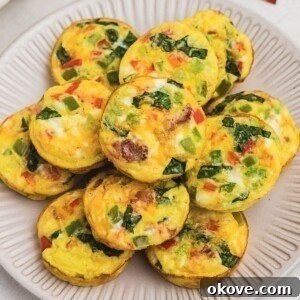 Bright yellow egg bites with red and green chopped bell peppers baked inside, on a round cream plate.