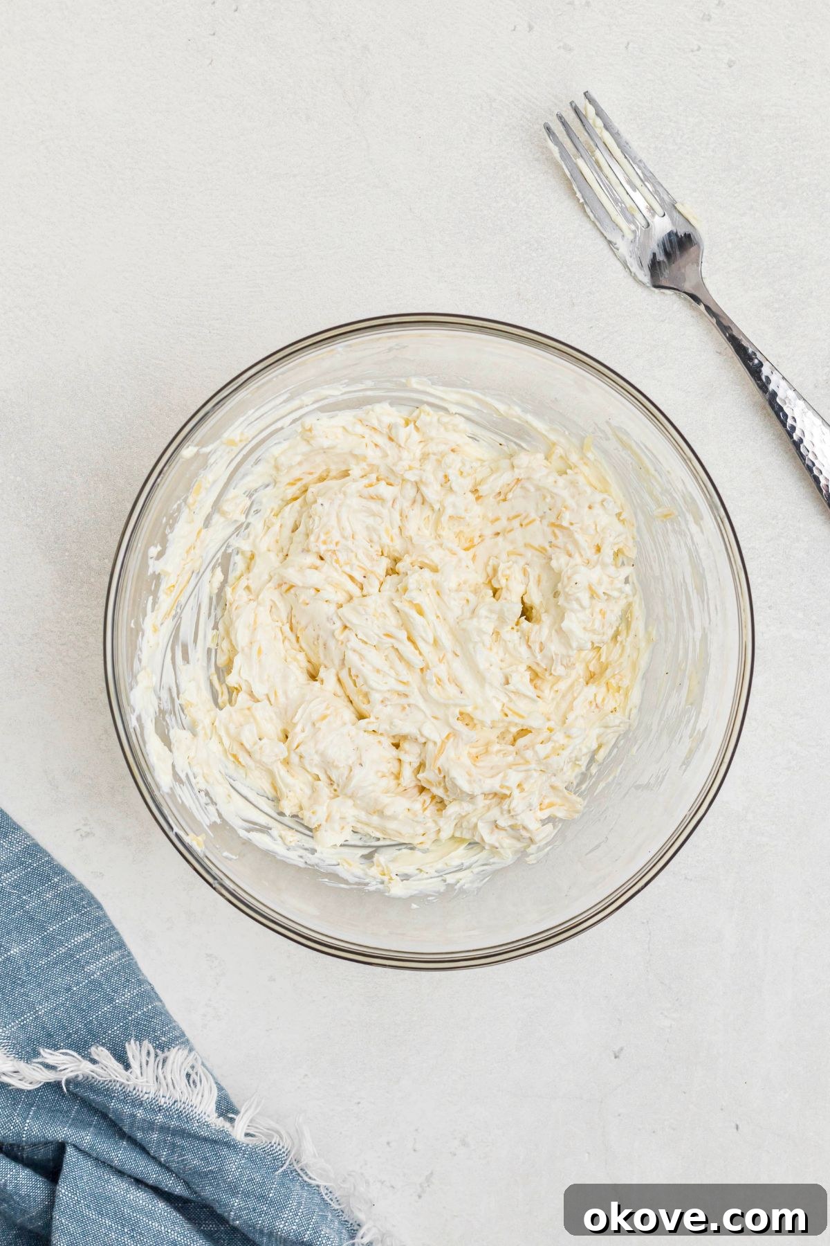 Medium clear glass bowl with cream cheese, parmesan cheese, and other ingredients, mixed together. 
