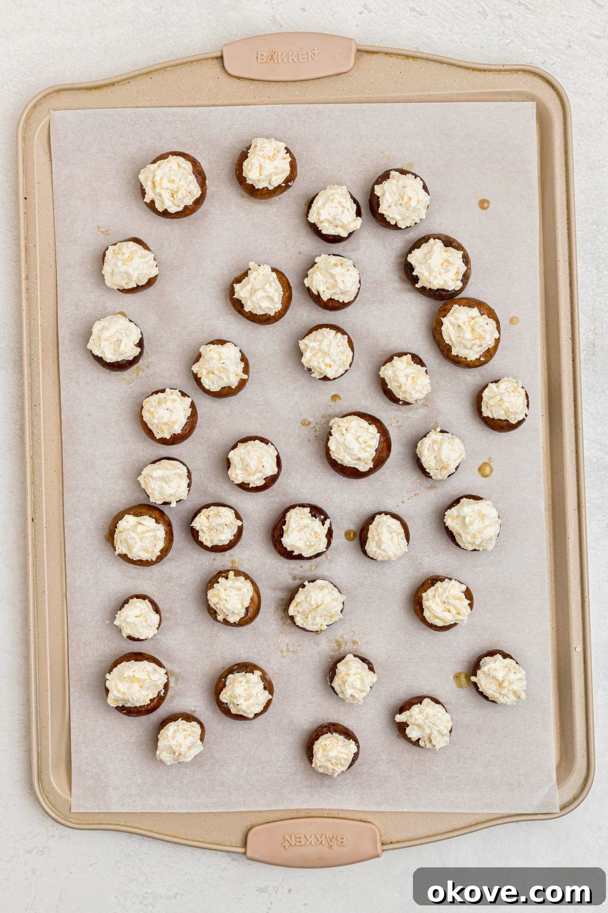 Mushrooms stuffed with cream cheese mixture on a lined baking sheet.
