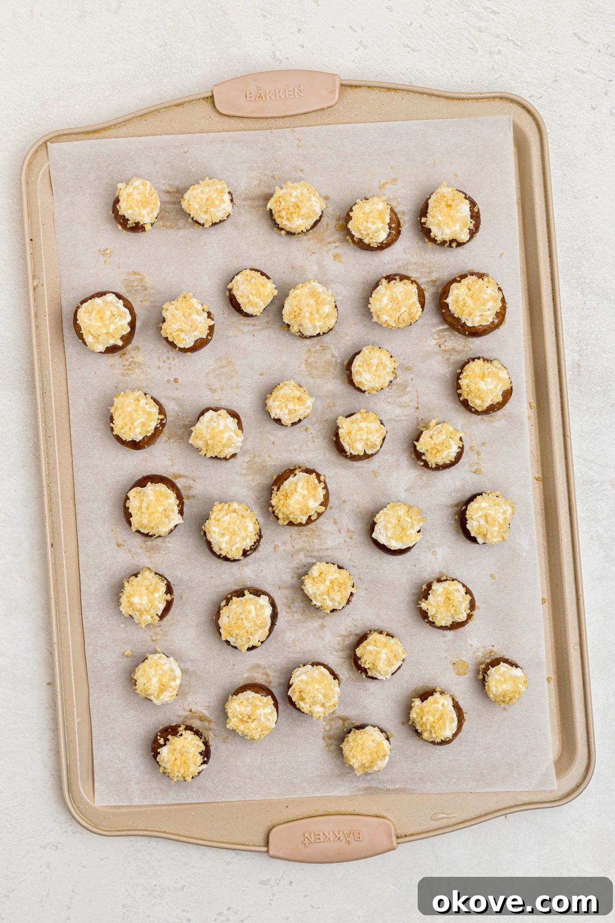 Mushrooms stuffed with cream cheese mixture, then topped with breadcrumbs and olive oil, on a baking sheet lined with parchment paper before baking. 