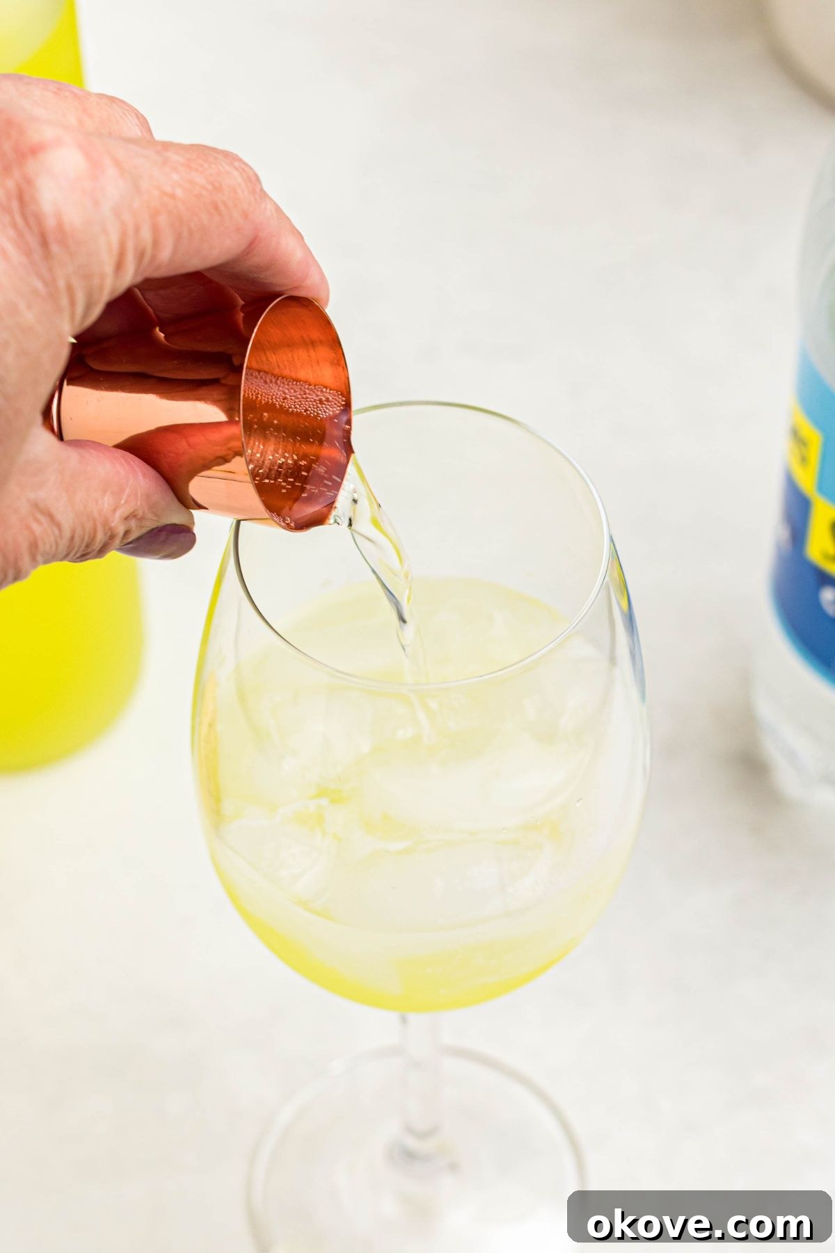 Limoncello Fizz 6 Mixing soda water and prosecco with limoncello in a clear wine glass, showing the layering of ingredients.