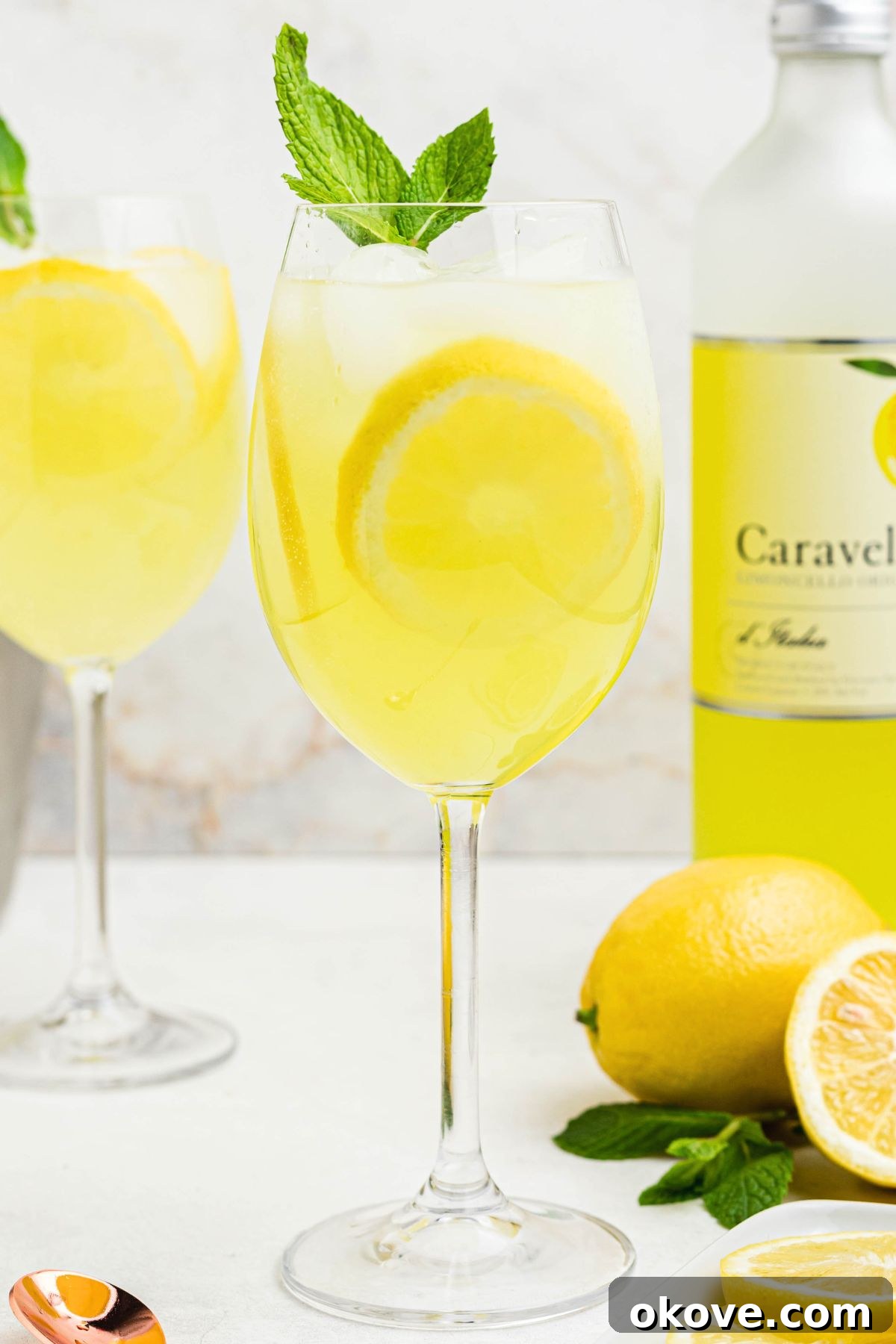 Limoncello Fizz 3 Glass of yellow limoncello spritz, topped with a sprig of mint and a lemon slice garnish.