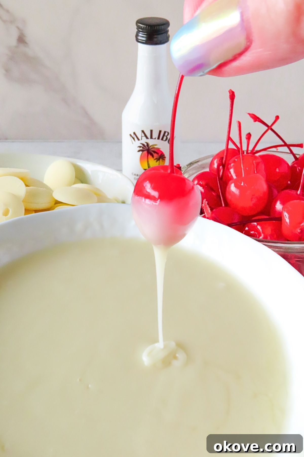 Bright red cherry being dipped into white melting chocolates. 