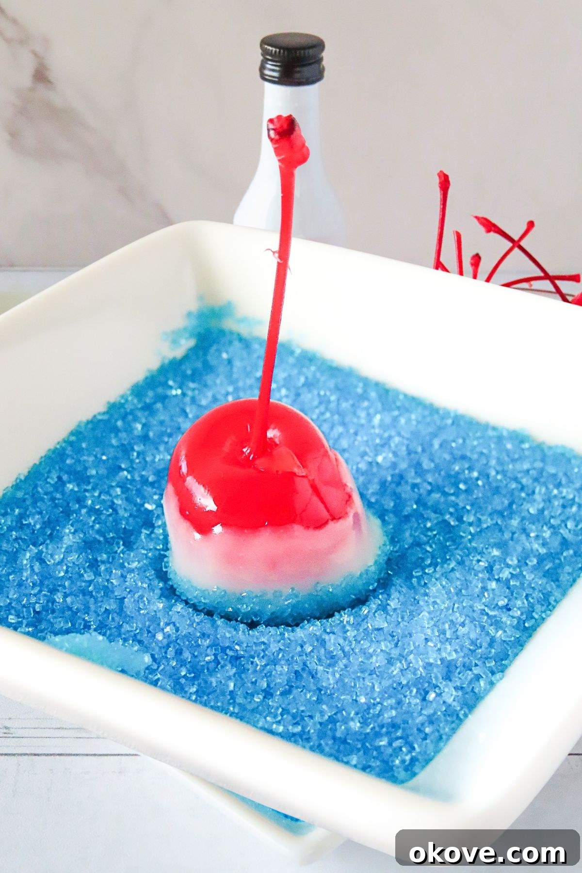 Red cherry with a stem, coated in white chocolate, then dipped into blue sanding sugar. 
