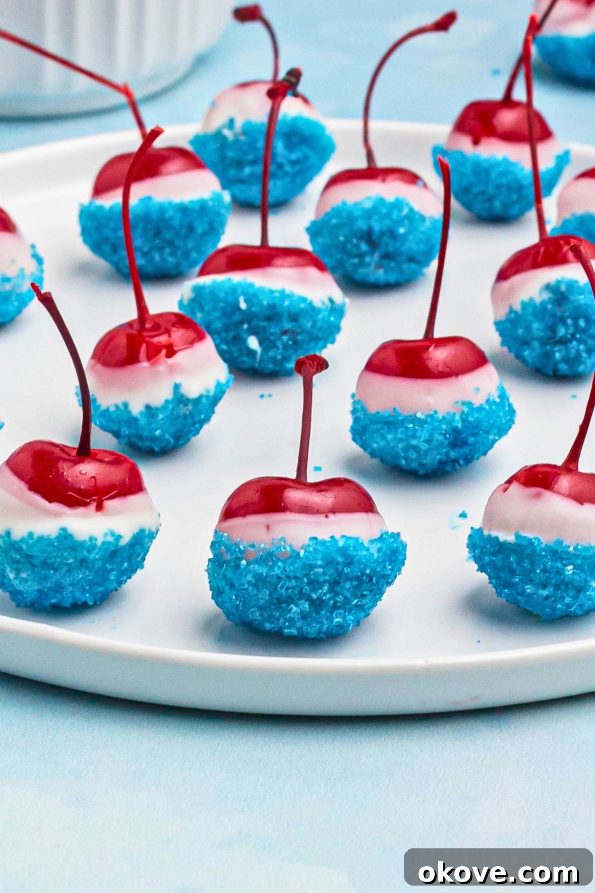 Cherries coated in white chocolate, then dipped in blue sanding sugar, on a white round plate. 