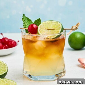 Rum and other ingredients, mixed together to make a Mai Tai, in a clear half glass, topped with a cherry and lime slice as a garnish.