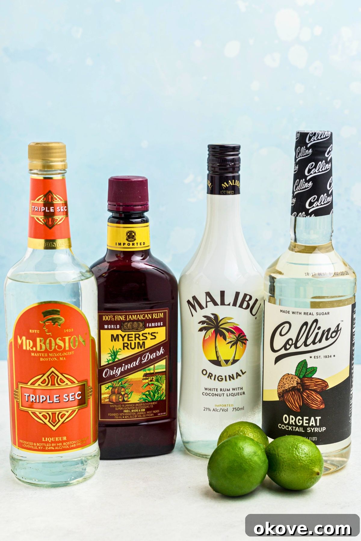 Mai Tai: Sip of the South Seas 3 Bottles of light rum, dark rum, Orgeat syrup, and Triple Sec, with fresh limes scattered on a rustic wooden table, ready for cocktail preparation.