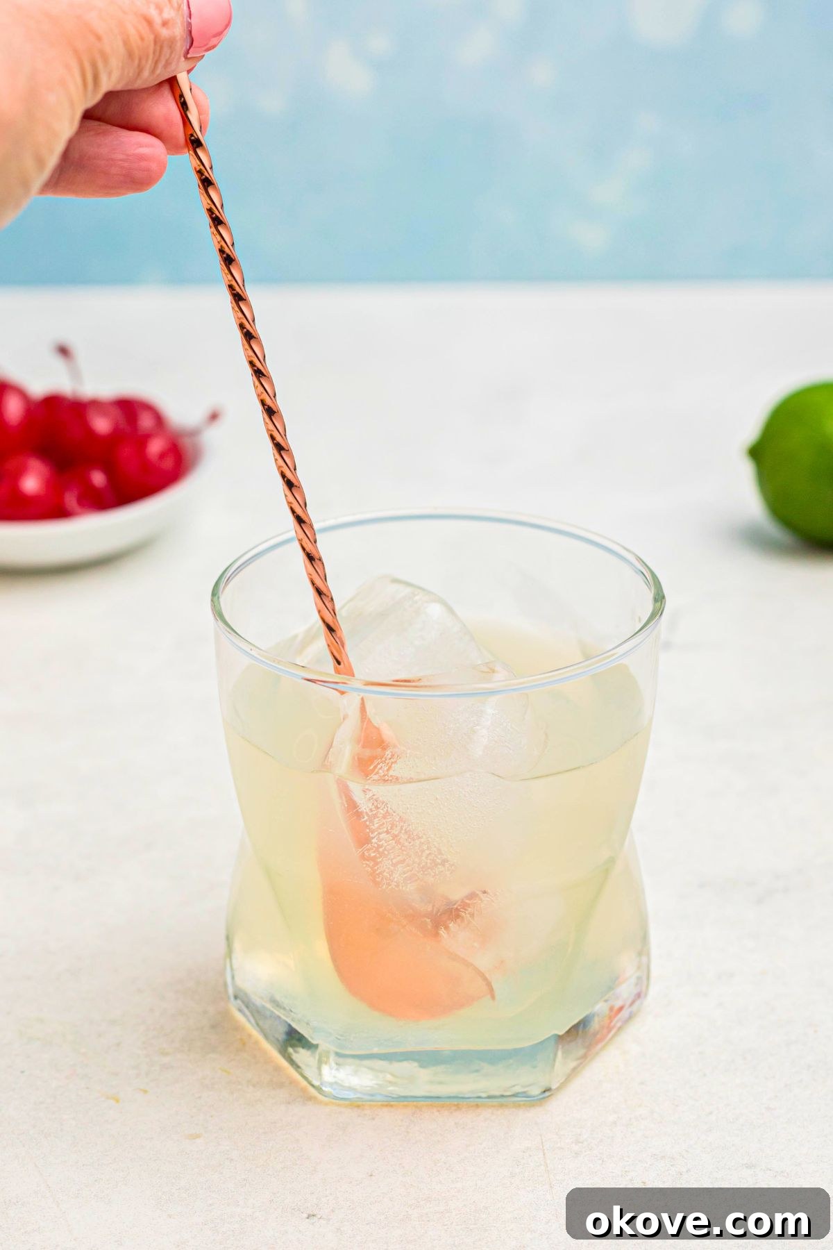 Mai Tai: Sip of the South Seas 5 A rose gold spoon stirring the vibrant ingredients in a clear glass filled with ice, blending the flavors of the Mai Tai.
