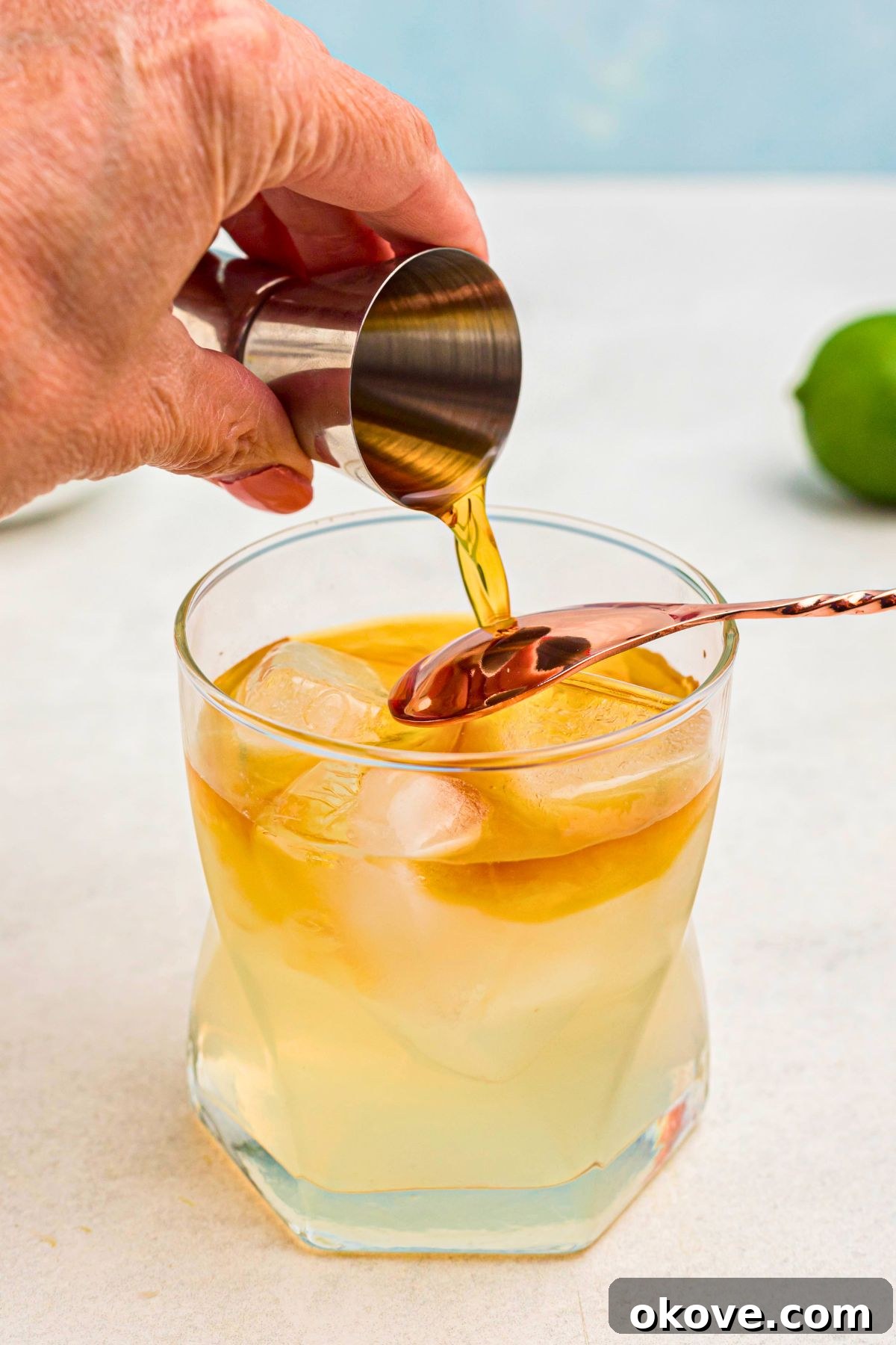 Mai Tai: Sip of the South Seas 6 Dark rum being meticulously poured over the back of a spoon, creating a distinct, visually appealing layer on top of a Mai Tai in a clear glass.