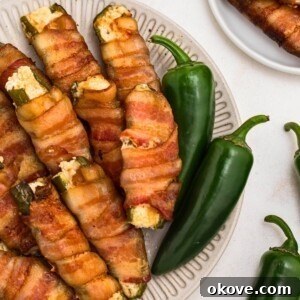 Fourth of July Recipes for a Memorable BBQ & Fireworks Night 11 Crispy bacon wrapped jalapenos filled with cheese, stacked on a white plate.