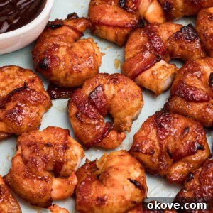 Crispy Bacon-Wrapped Shrimp Skewers with Garlic Butter Dip 9 Crispy bacon wrapped around shrimp, coated with BBQ sauce mixture, on a light green plate with lemon slices and serving tongs on the table.