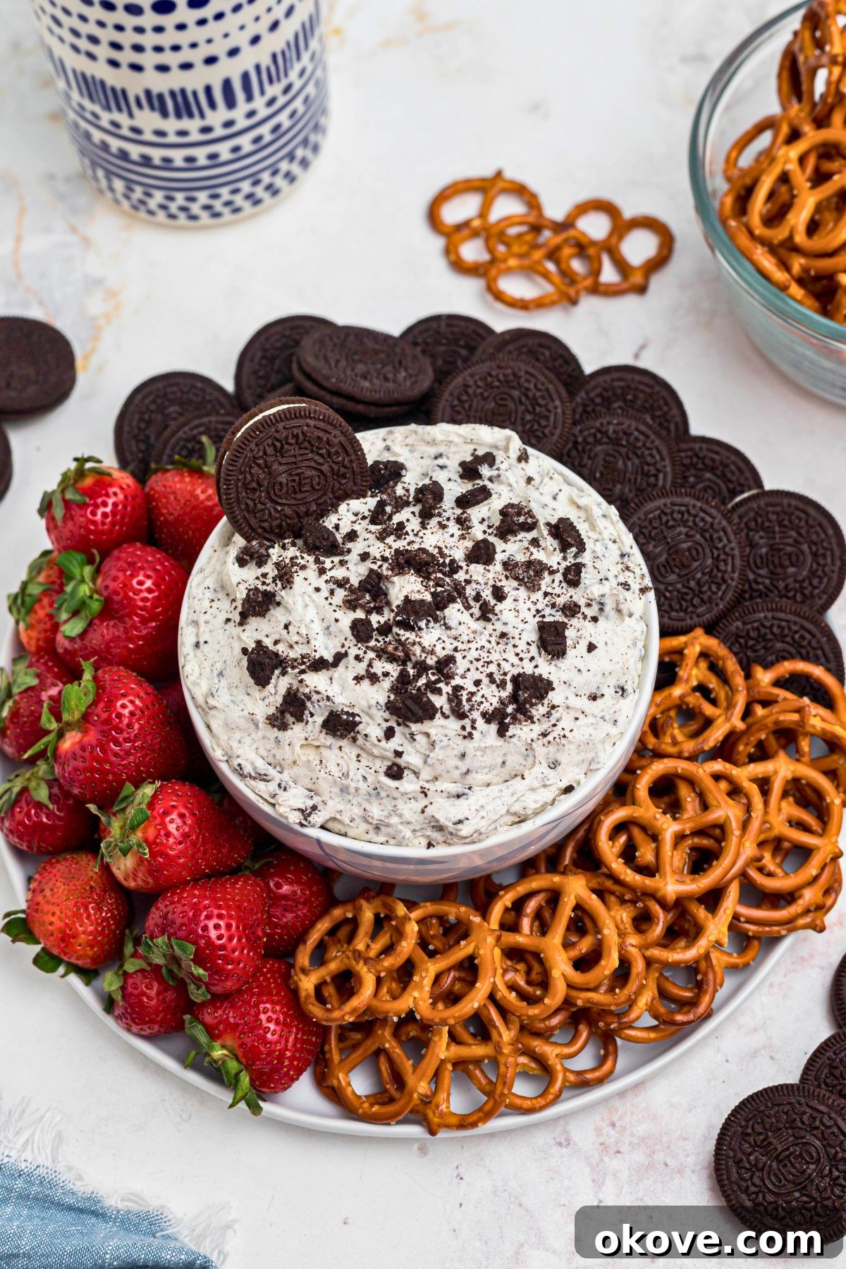 Creamy Oreo Dessert Dip for Parties and Snacks 2 Strawberries, pretzels, and chocolate cookies, on a round white plate, around a cookies and cream Oreo dip, on a marble table.